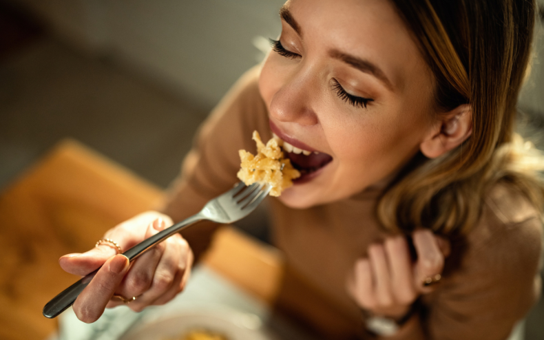 A woman eating a bowl of pasta.
