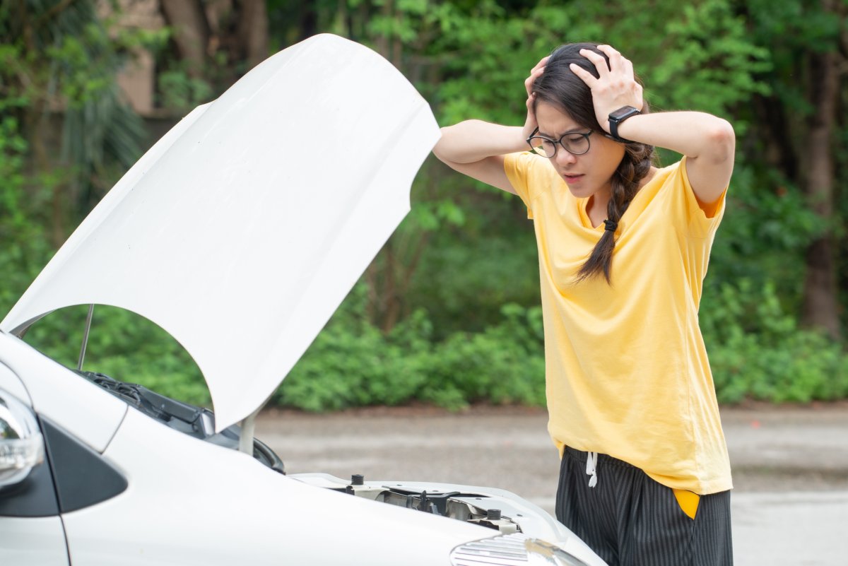 A teenager looks beneath her car hood