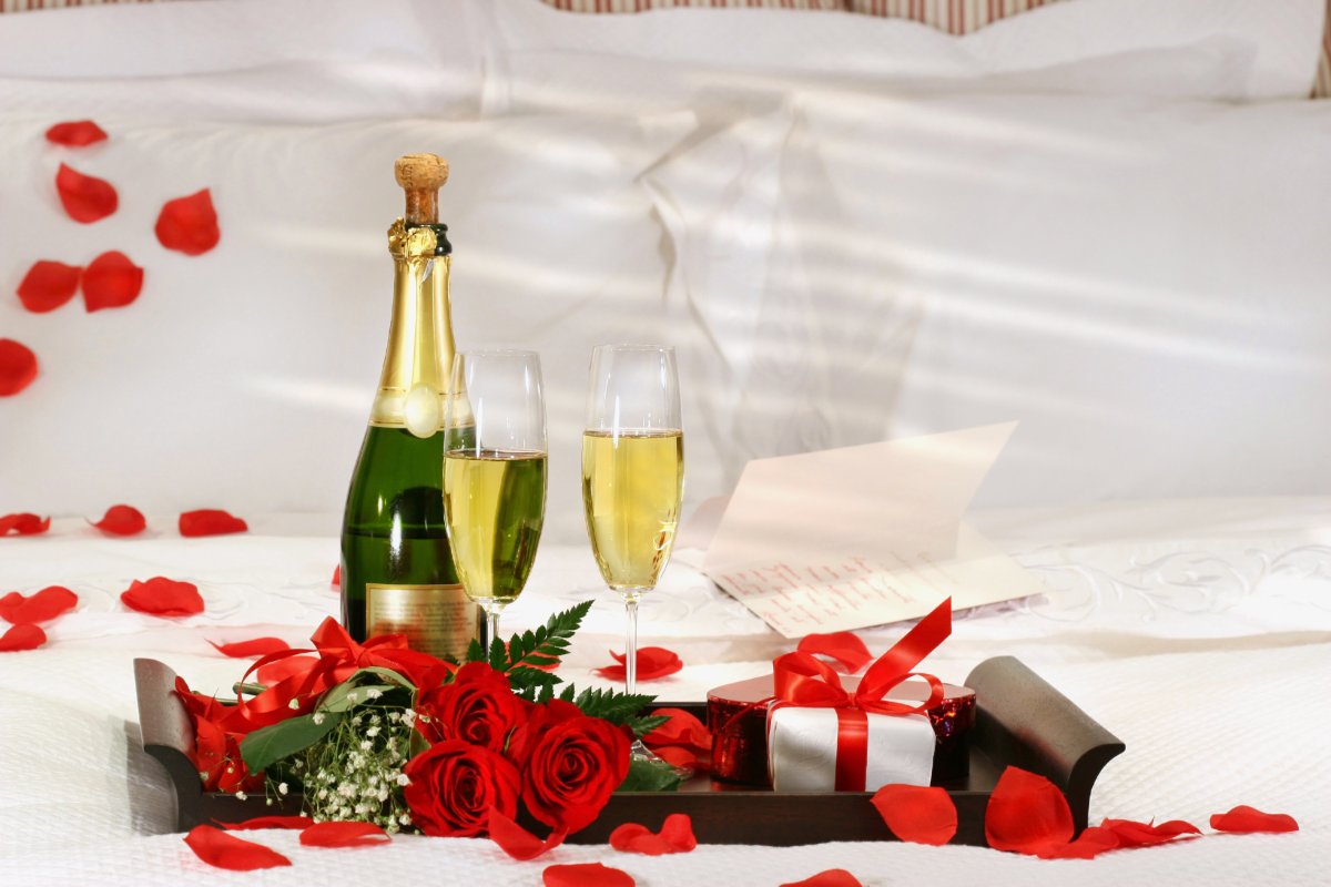 Champagne, roses and gift box on bed.