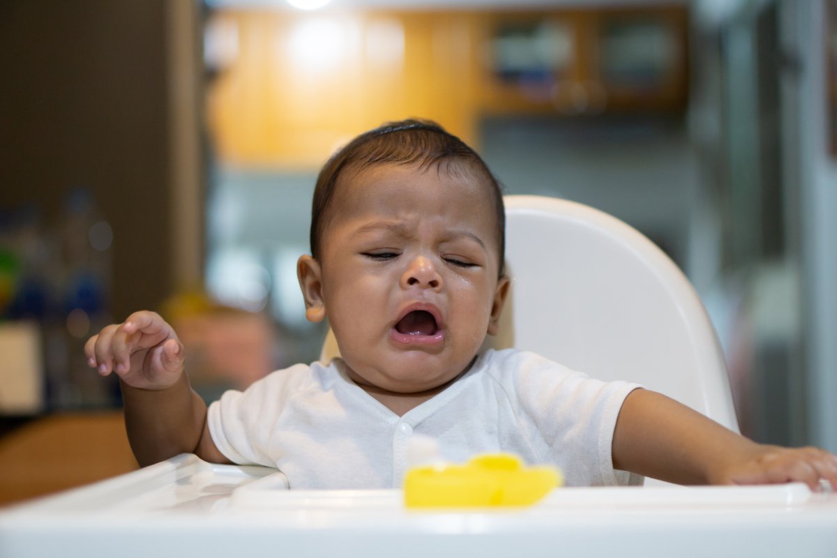 A baby cries in a high-chair