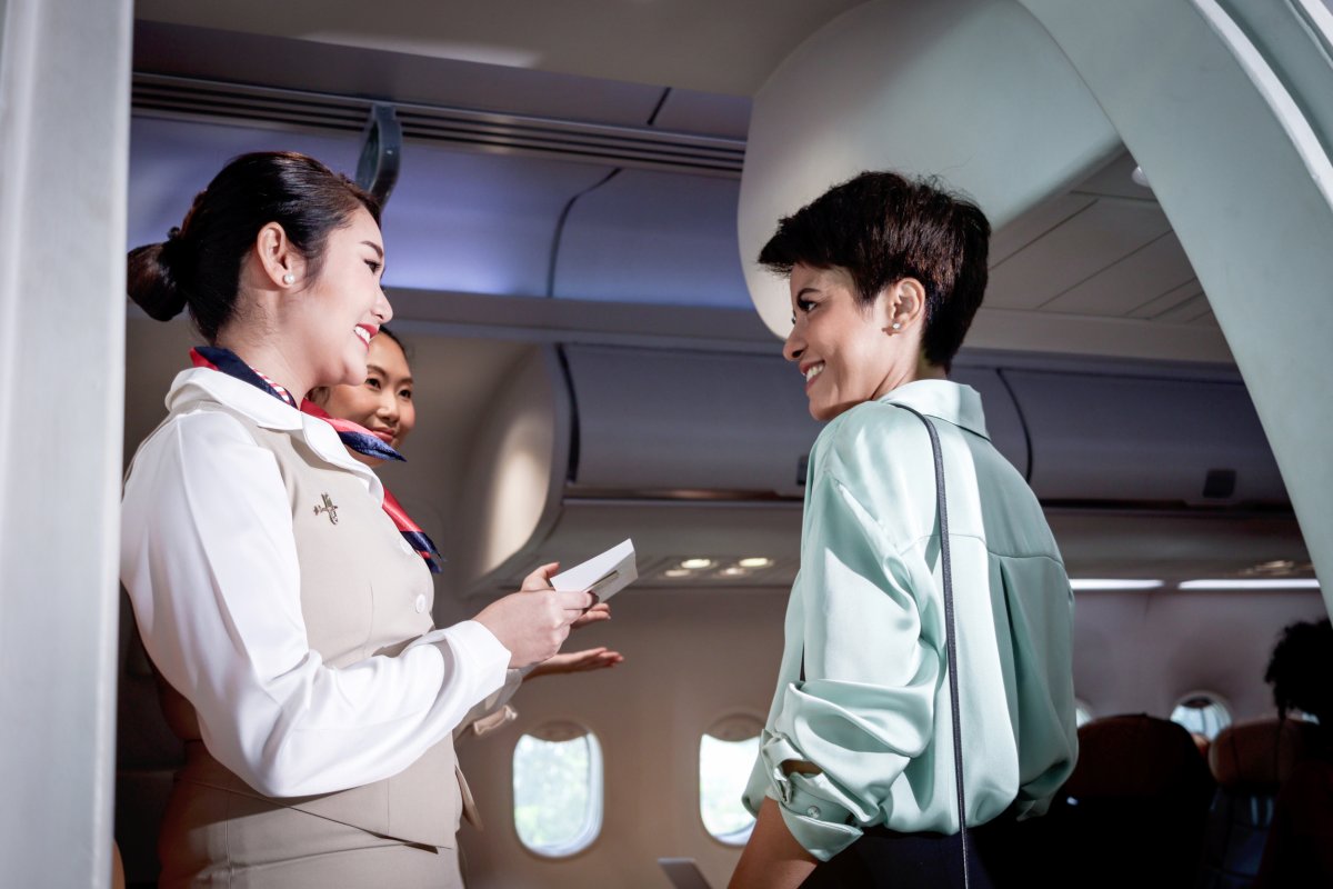Flight attendant greeting passenger on plane.