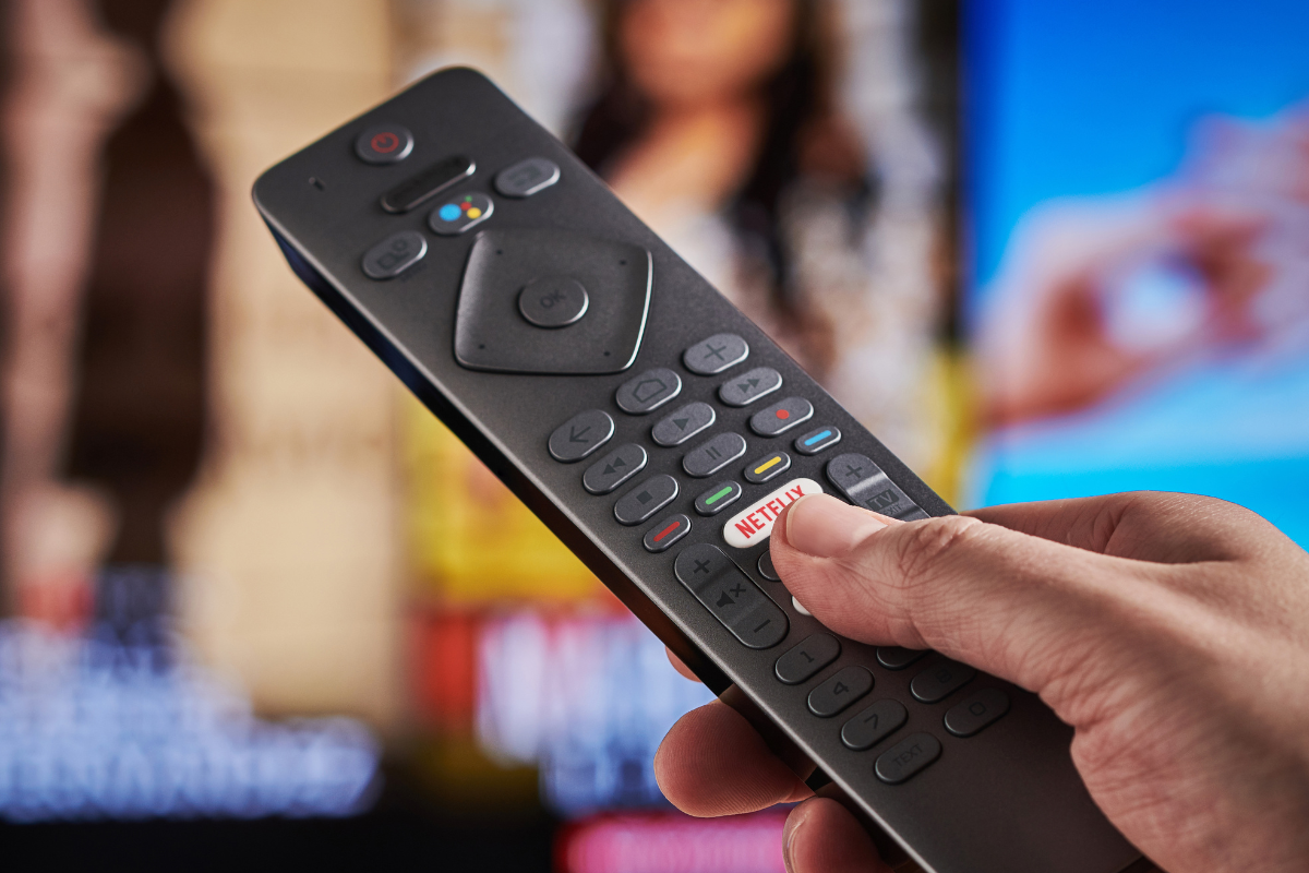 A man's hand pressing holding TV remote