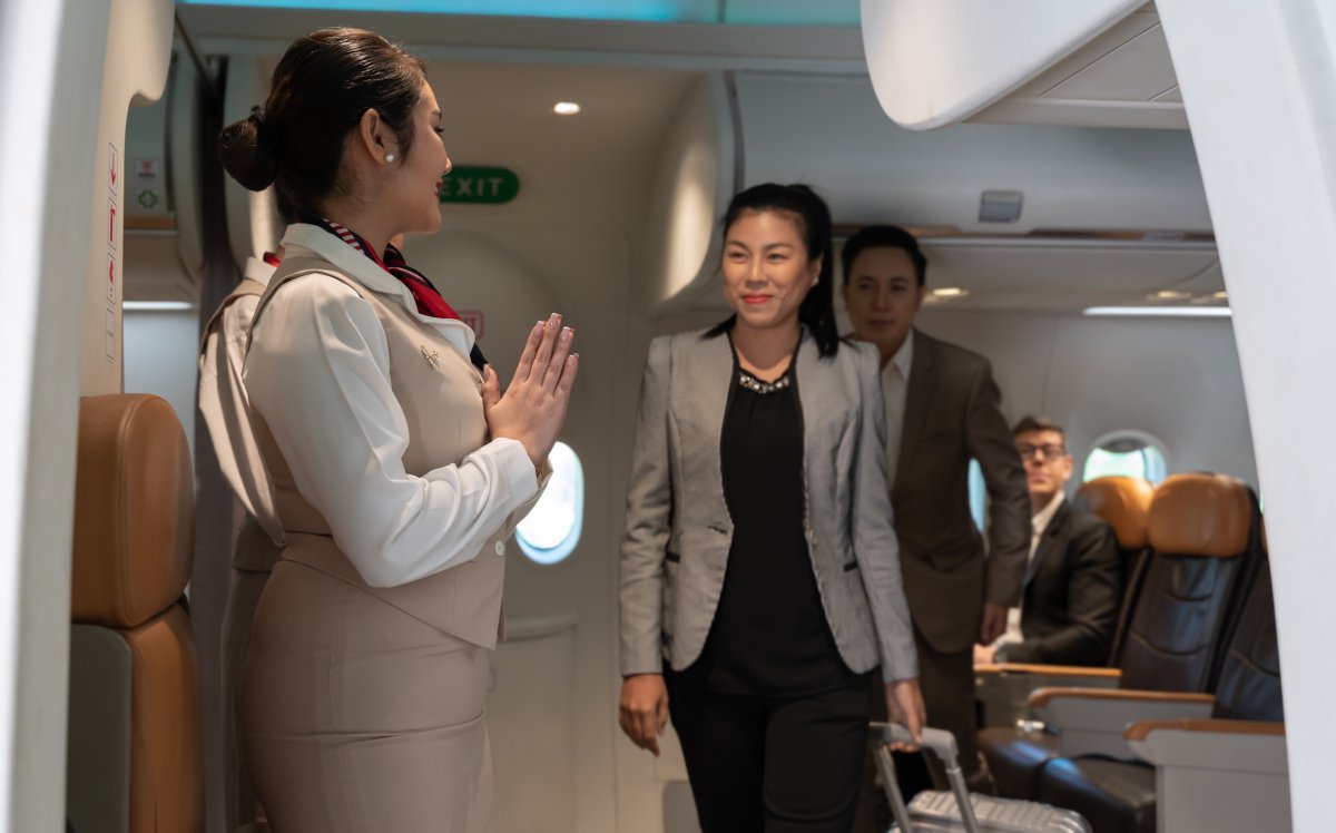 Flight attendants greeting passengers on plane.