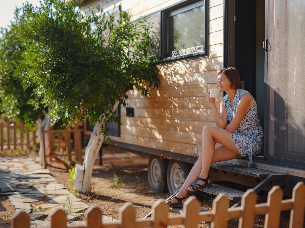 A woman sits outside a small house.