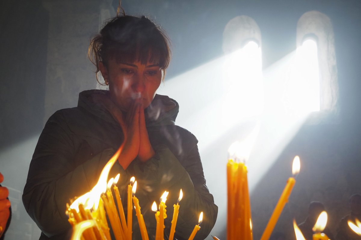 Una mujer enciende velas dentro de una iglesia.