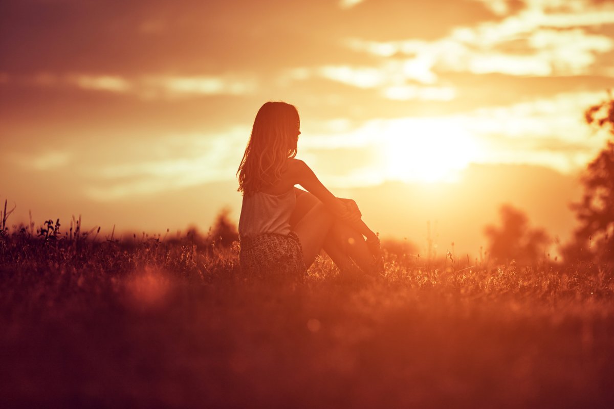 woman sitting in a field at sunset