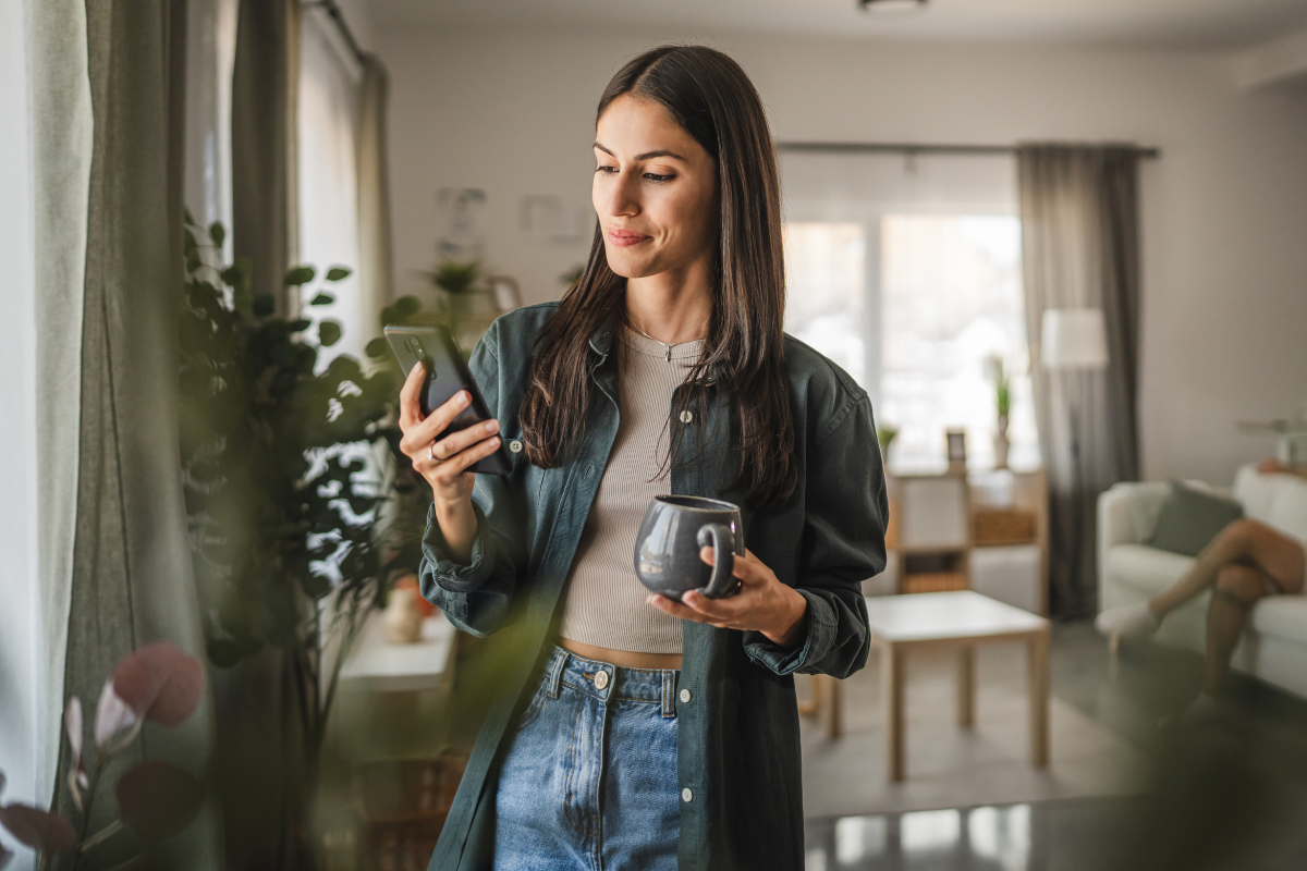 Woman Looks at Cell Phone, Holds Cup