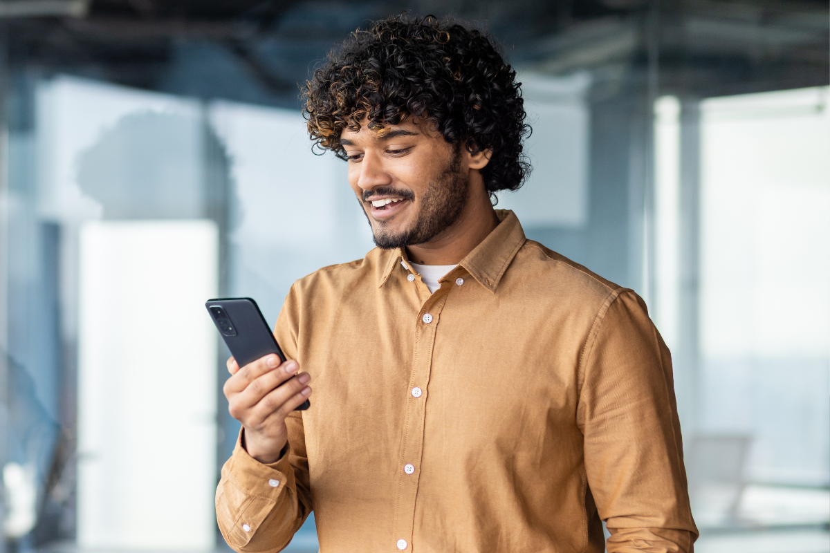 Man with curly hair smiling and holding cell phone