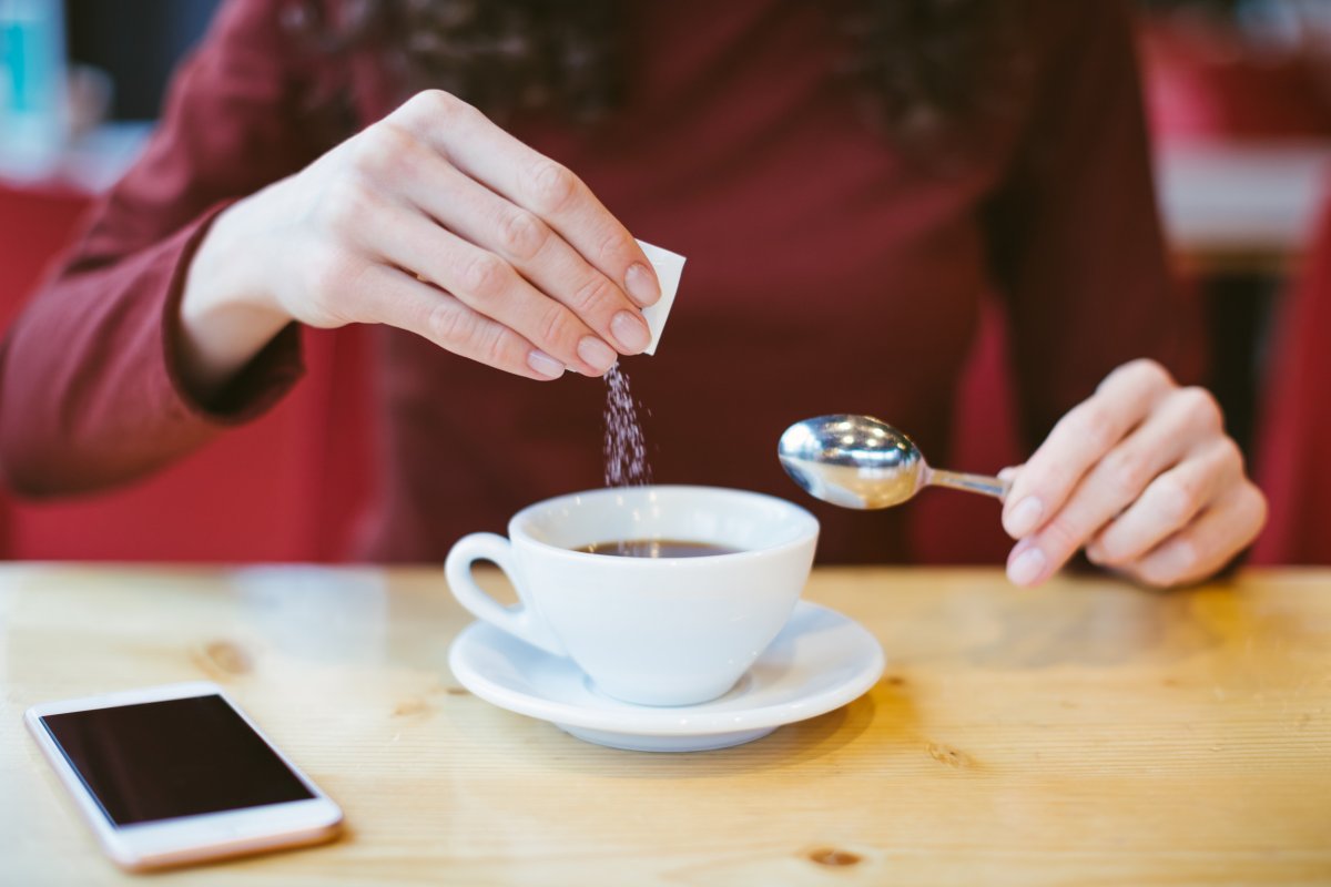 A woman pours sugar into coffee