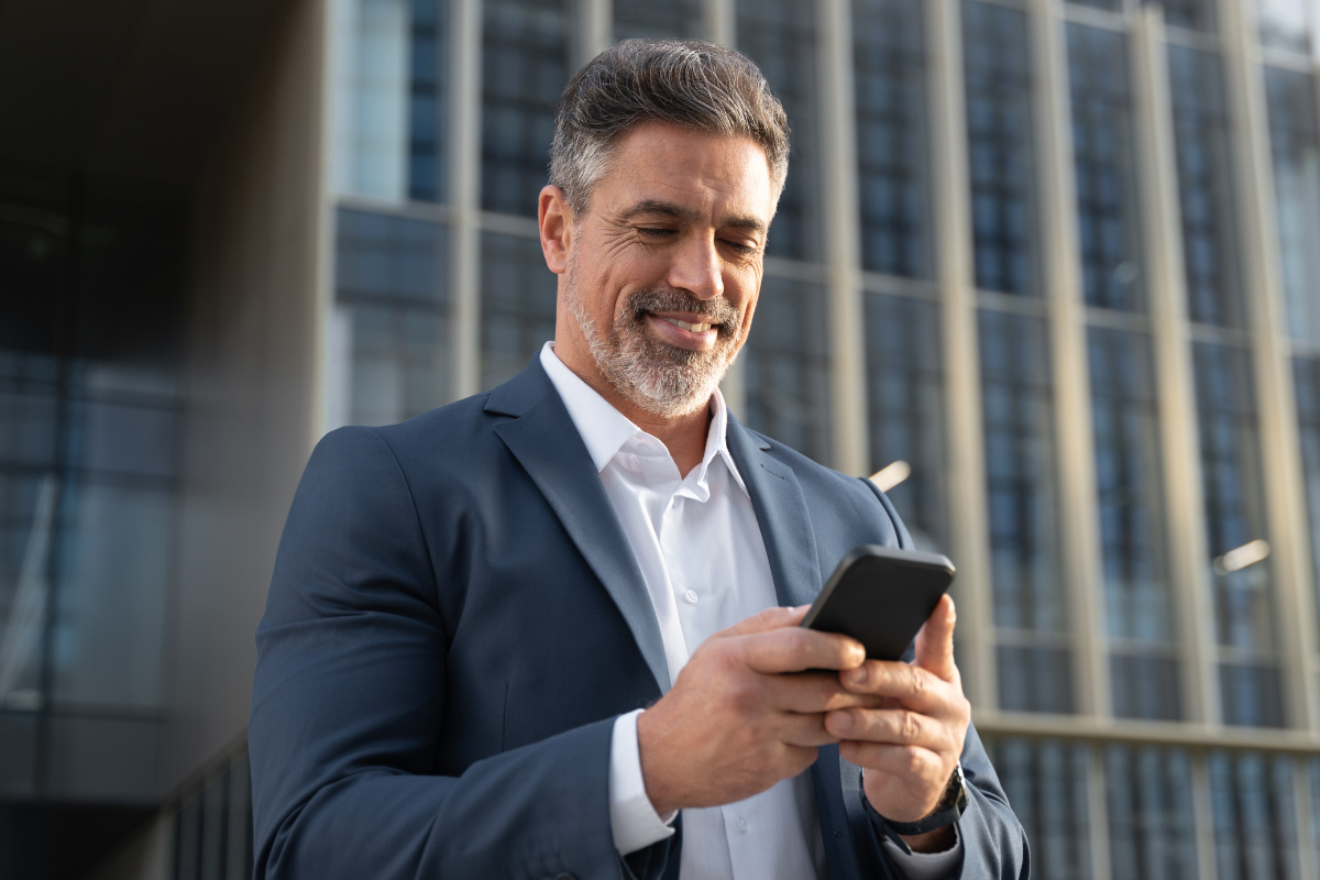 Businessman in suit smiles typing mobile phone