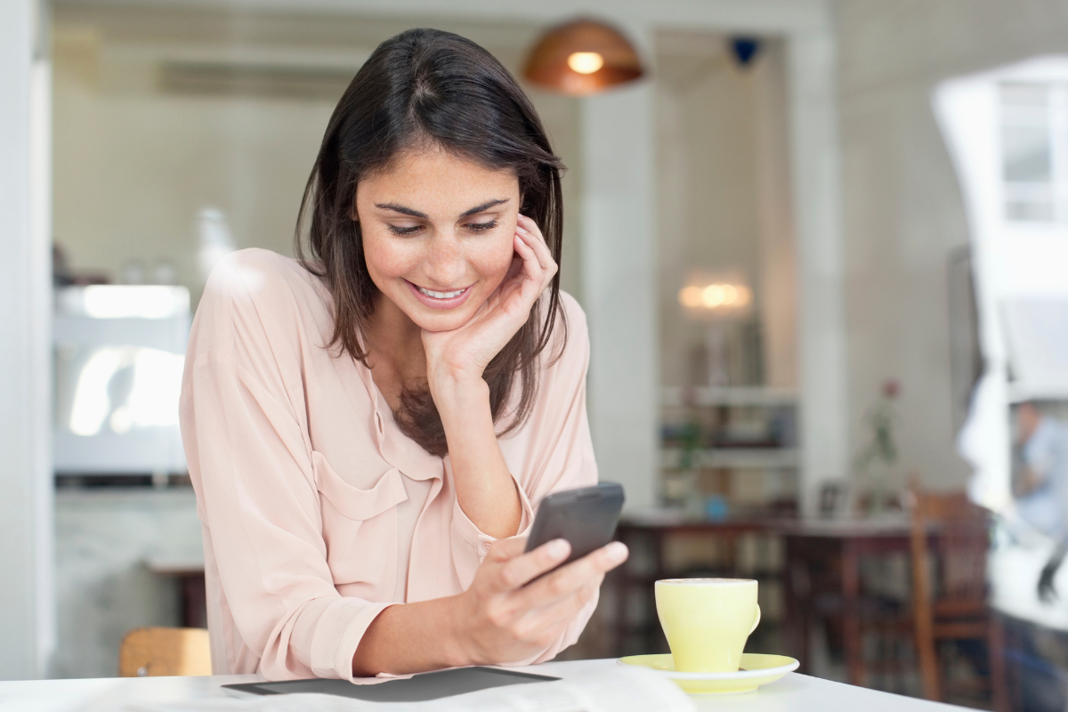 Woman drinking coffee and smiling holding her cell phone