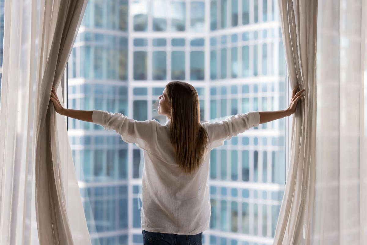 Woman standing near windows with curtain opened.