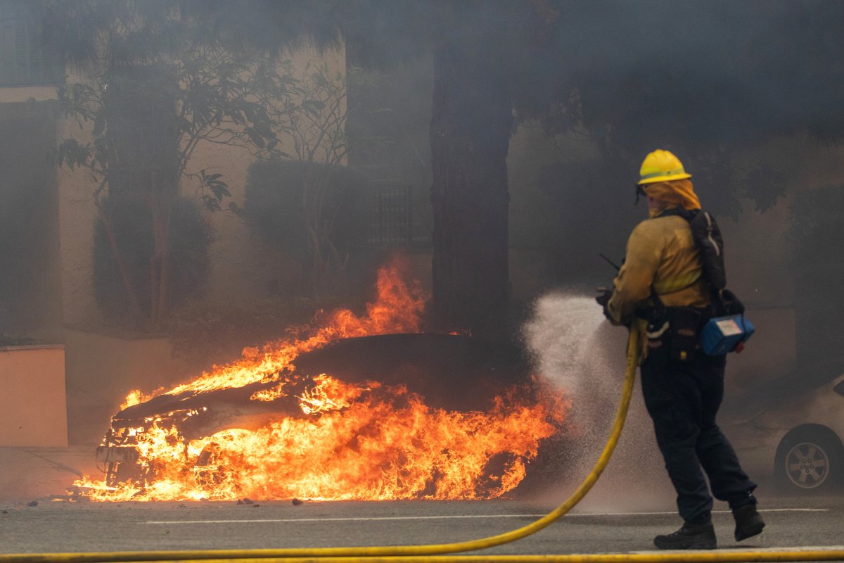 A firefighter sprays water at burning car