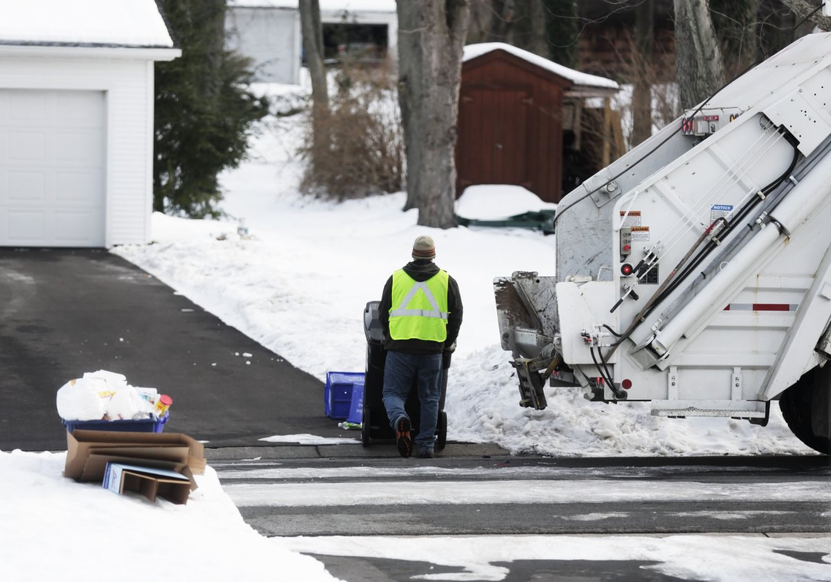 Worker moving bin near garbage truck.