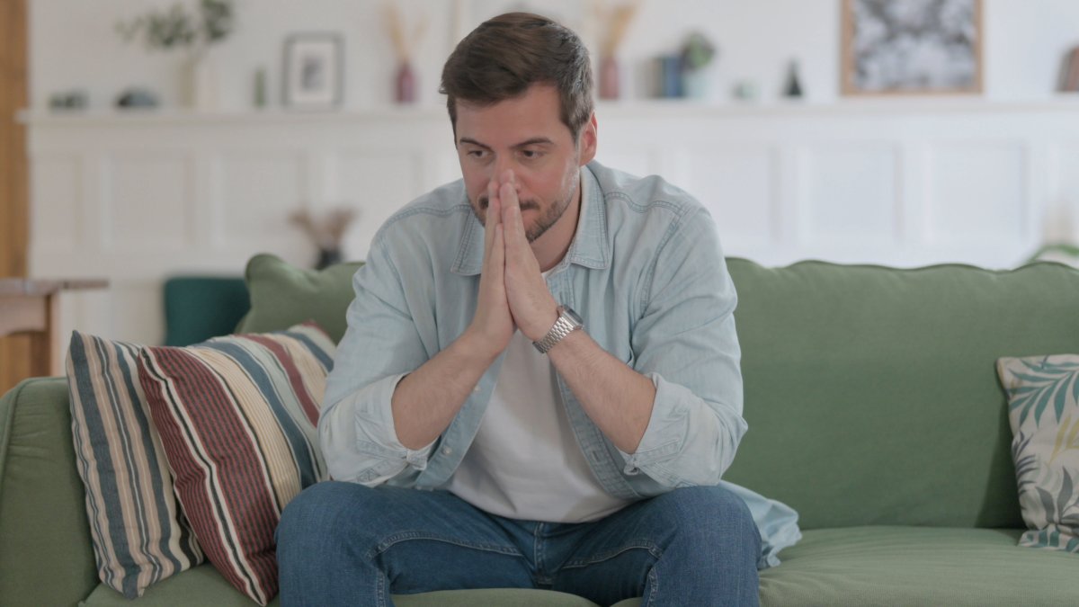 Man appearing stressed while sitting on couch.