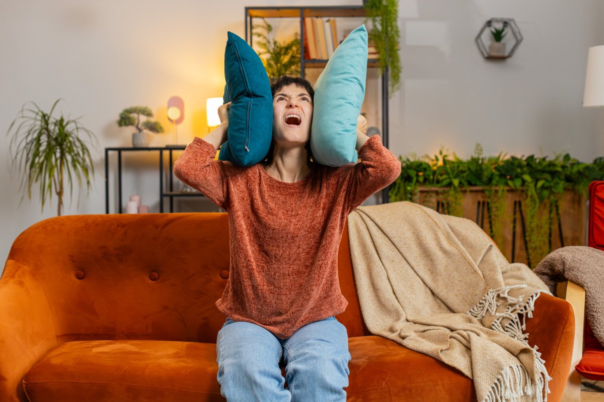 Woman holding cushions over ears on sofa.