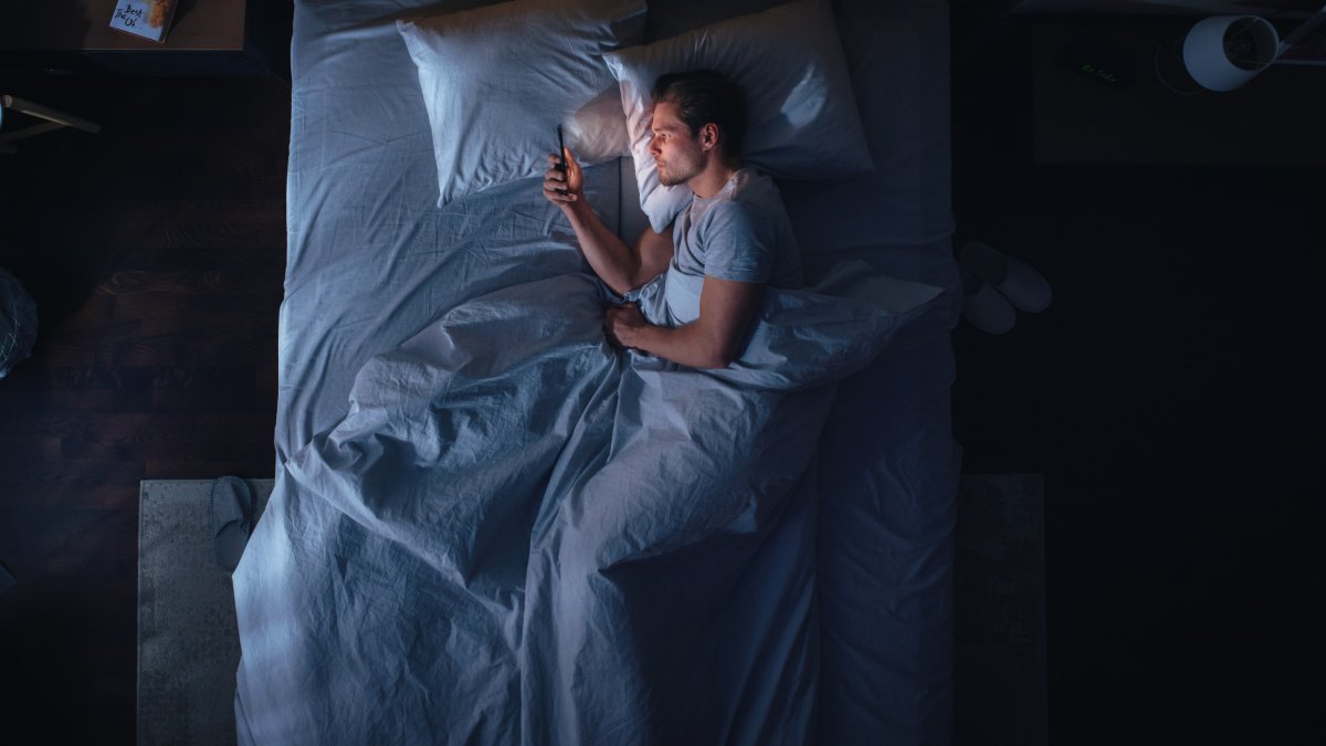 Young Man Lays In Bed With Phone