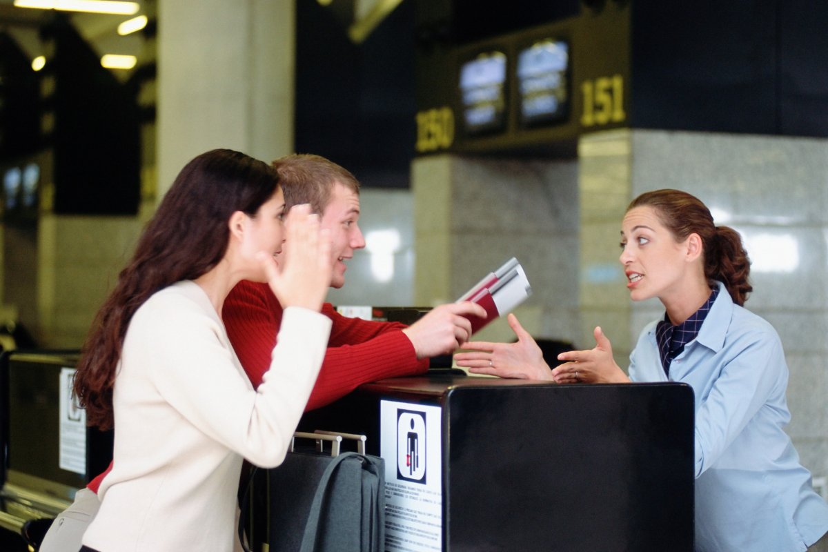 Passengers speaking to check-in agent at airport.