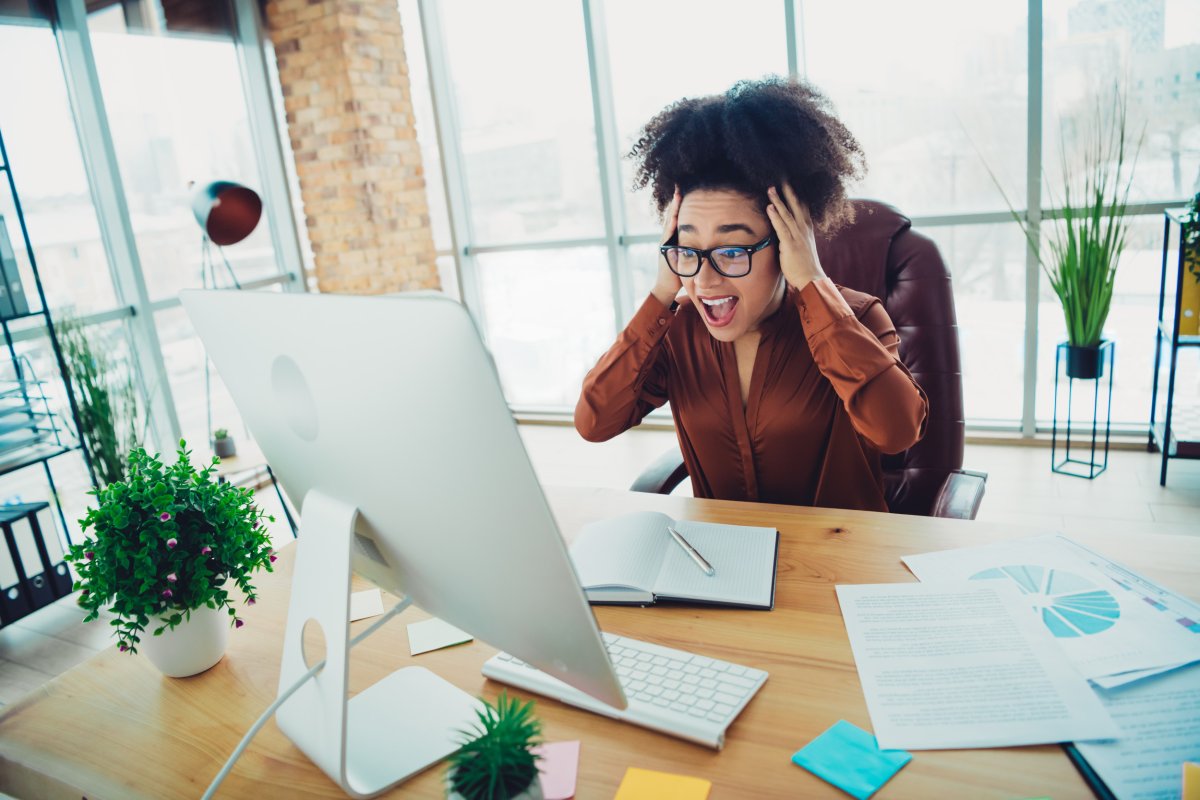 Woman shocked looking at computer at desk.