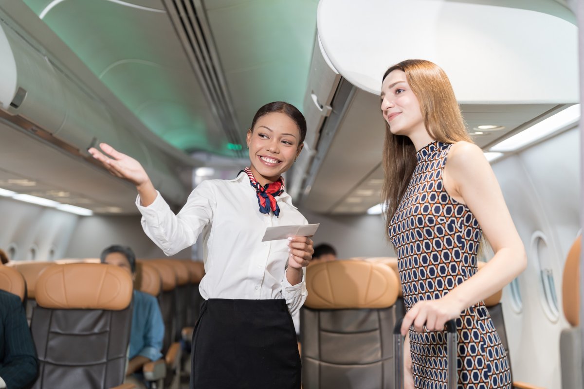 Flight attendant directing woman on plane.