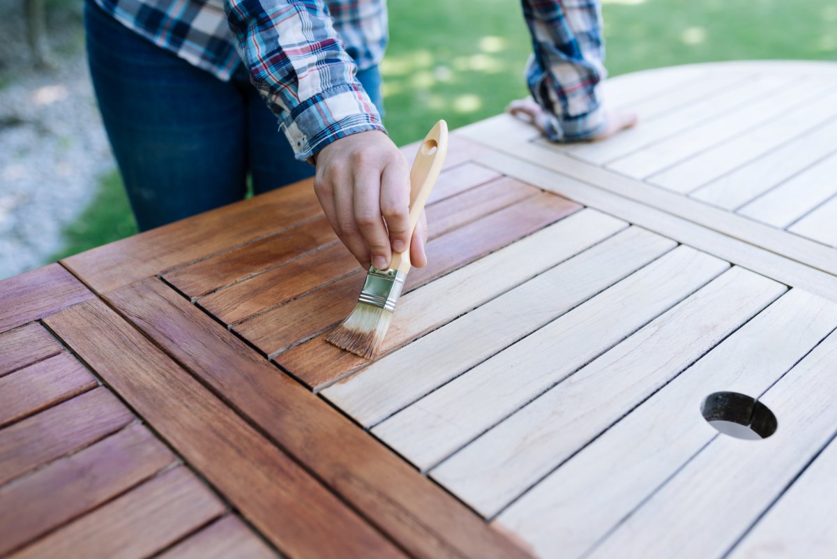 A person painting a wooden table outdoors.