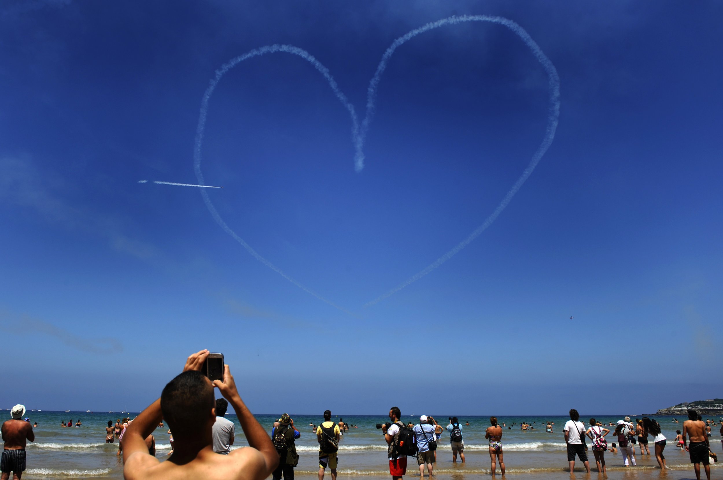 Beach goers watch a Spanish Air Force jet fly over a beach in Northern Spain