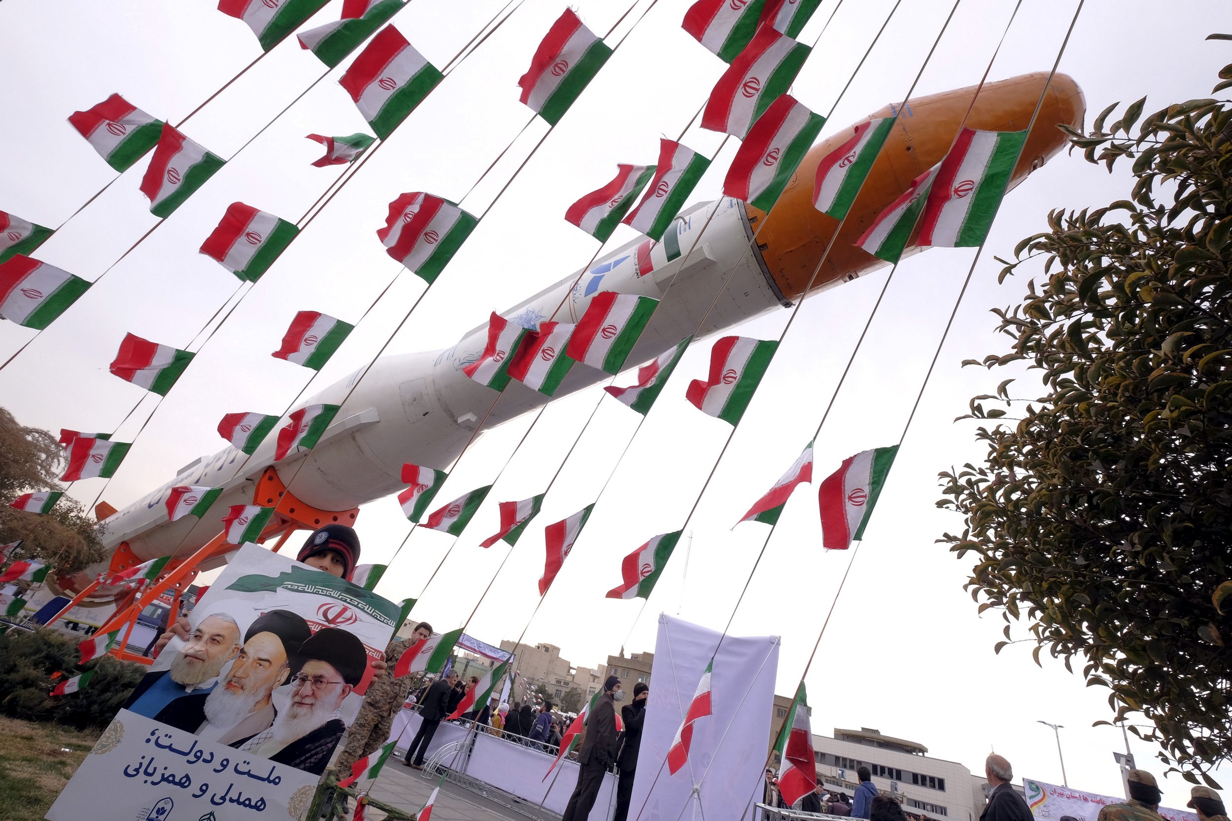 Iranian boy stands in front of missile surrounded by Iranian flags