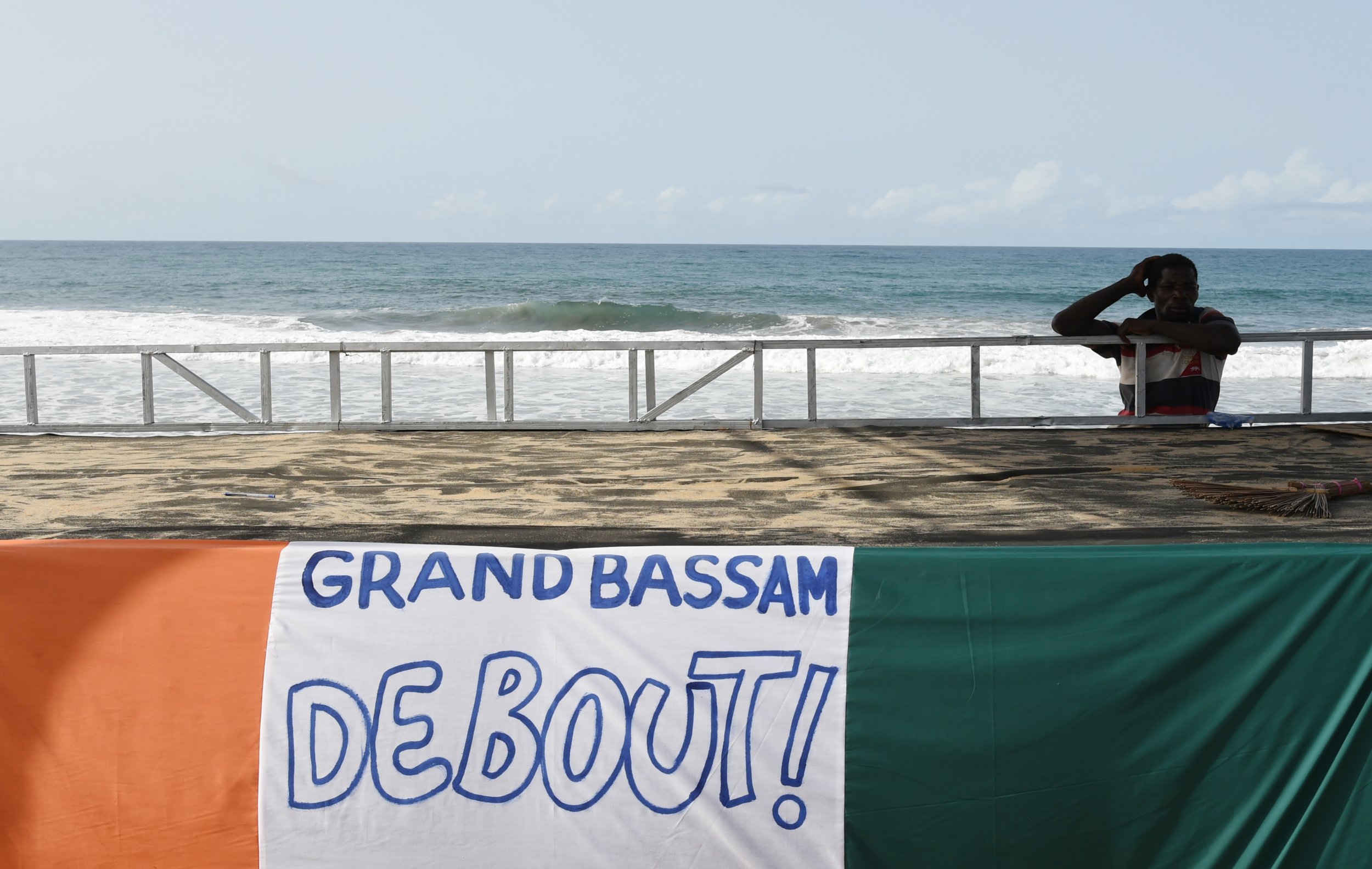 An Ivorian man stands near a Grand Bassam banner after an Al-Qaeda attack.