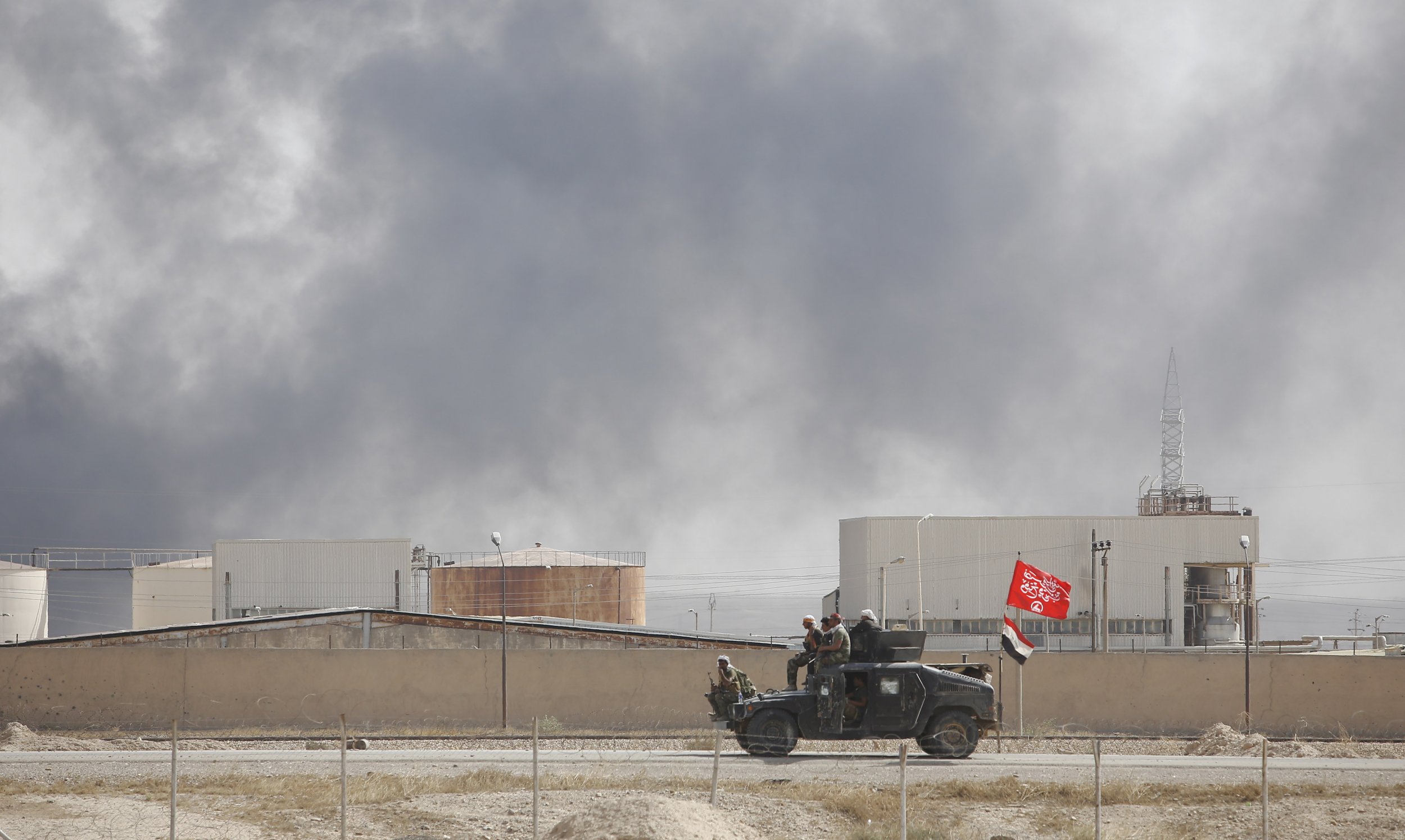 Iraqi fighters drive past oil refinery.