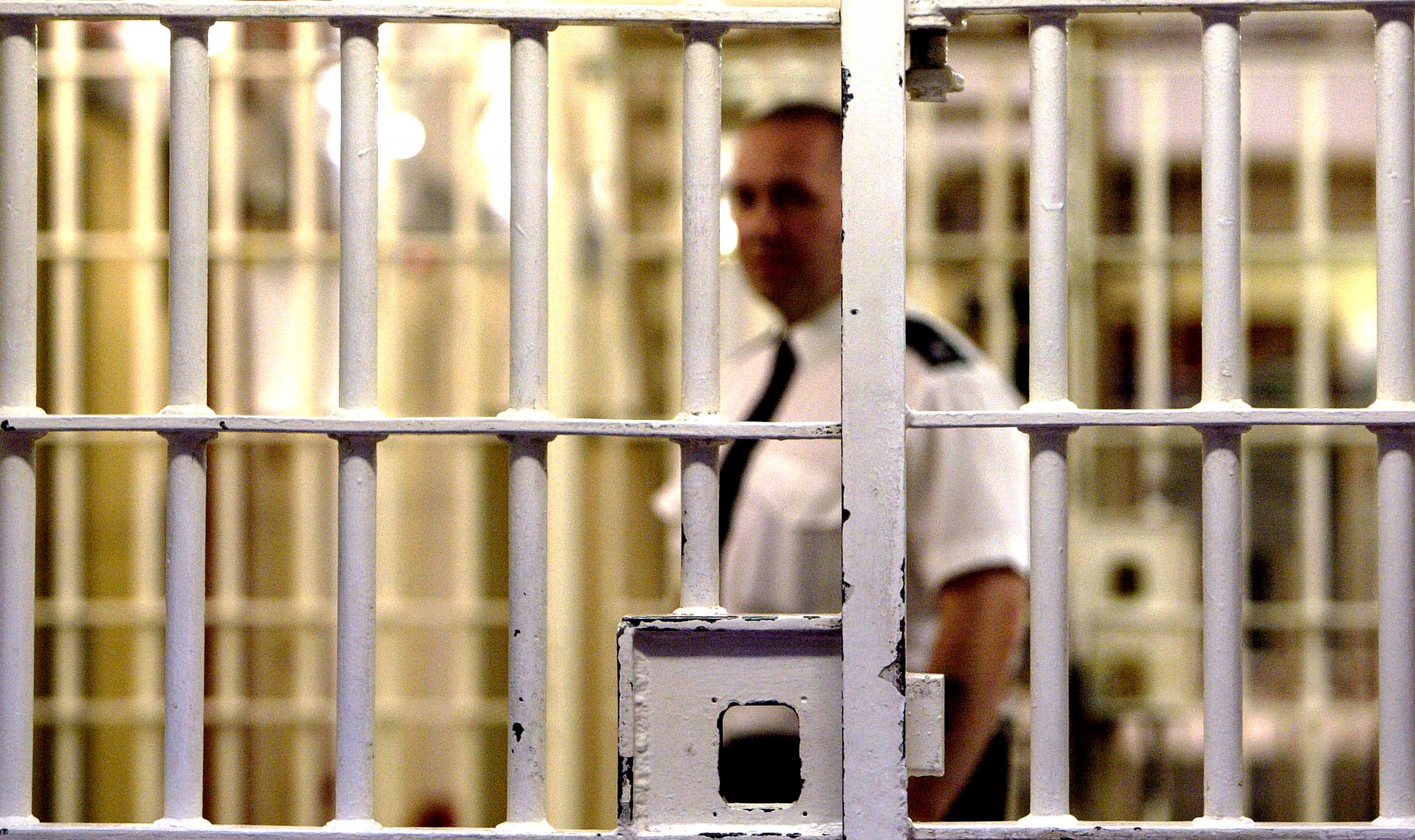 A prison warden stands in front of a cell