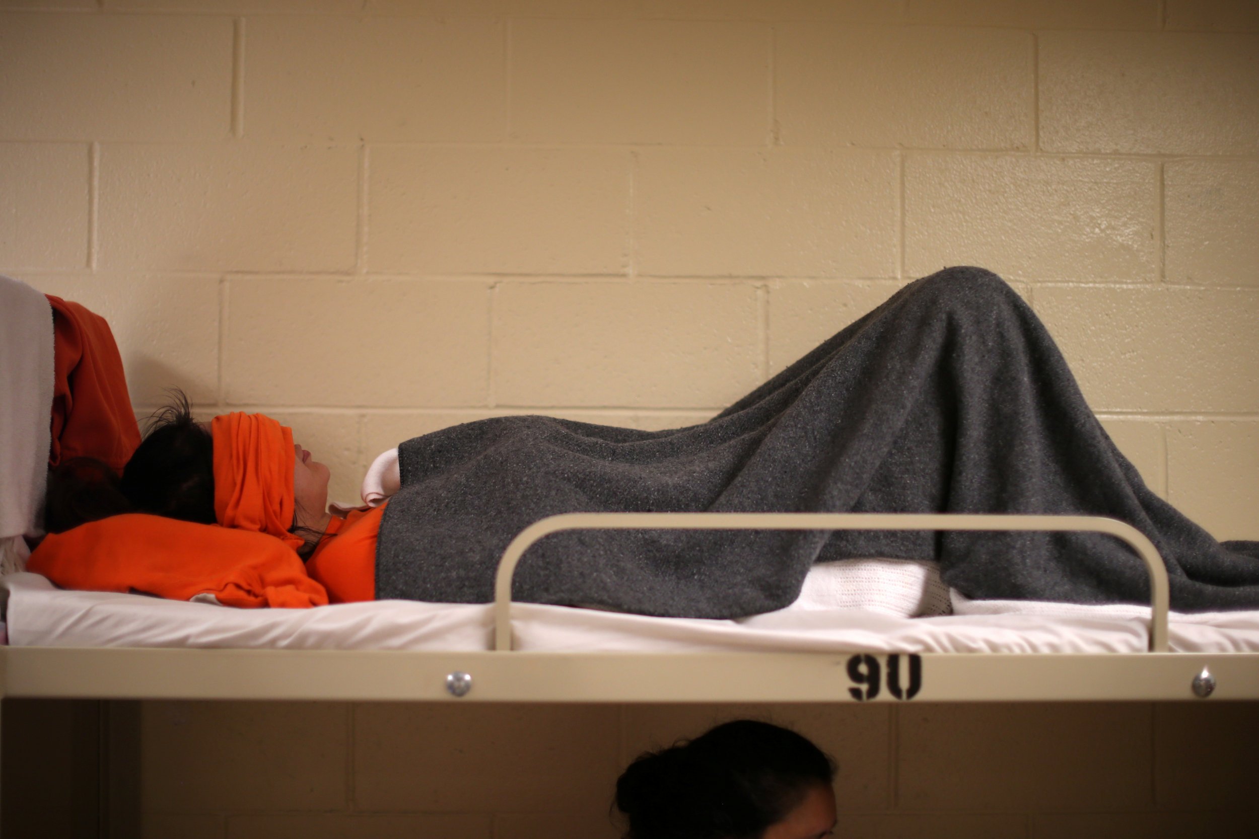 A woman lies on a bed at the Adelanto immigration detention center